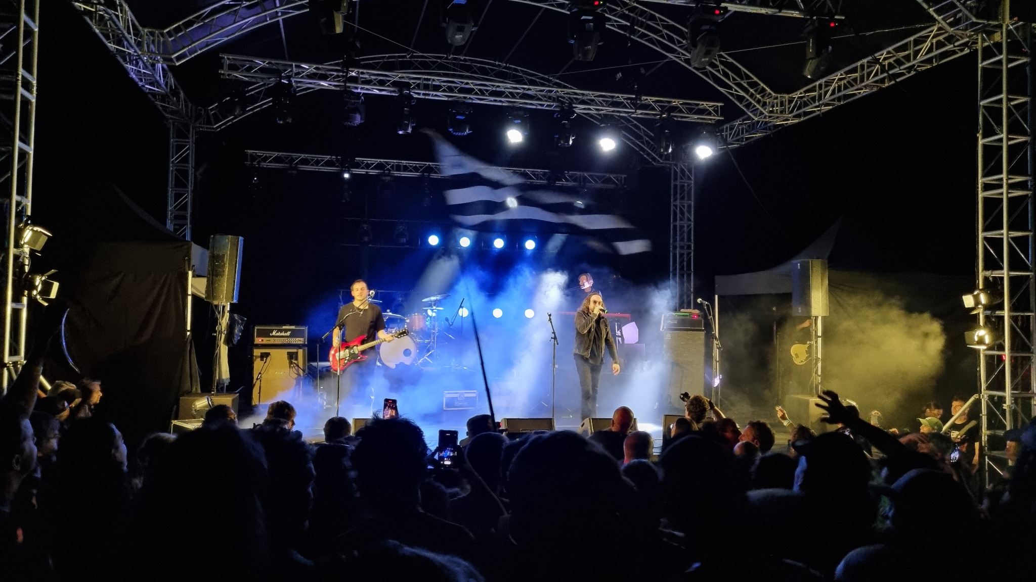 Concert rock sur la scène du festival, éclairée de bleu devant le public.